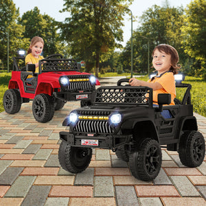 Two children playing with black and red toy jeeps on a paved path with greenery in the background.