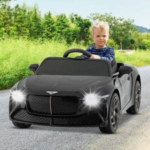 Child sitting in a black toy Bentley car on a road with greenery in the background