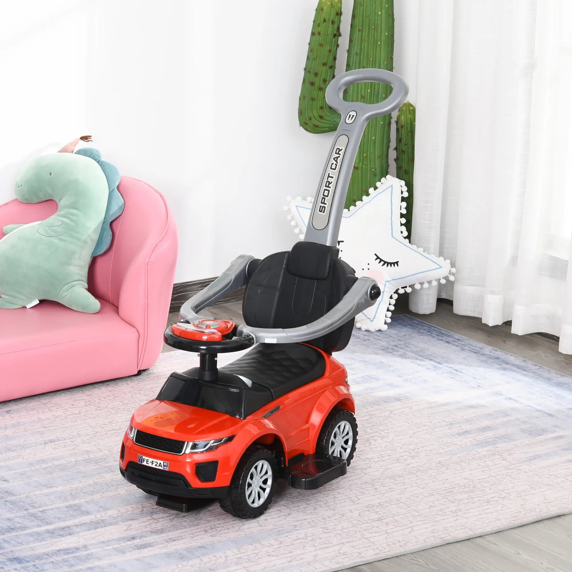 Red toy car with a steering wheel on a wooden floor, pink couch, and green plant in the background.