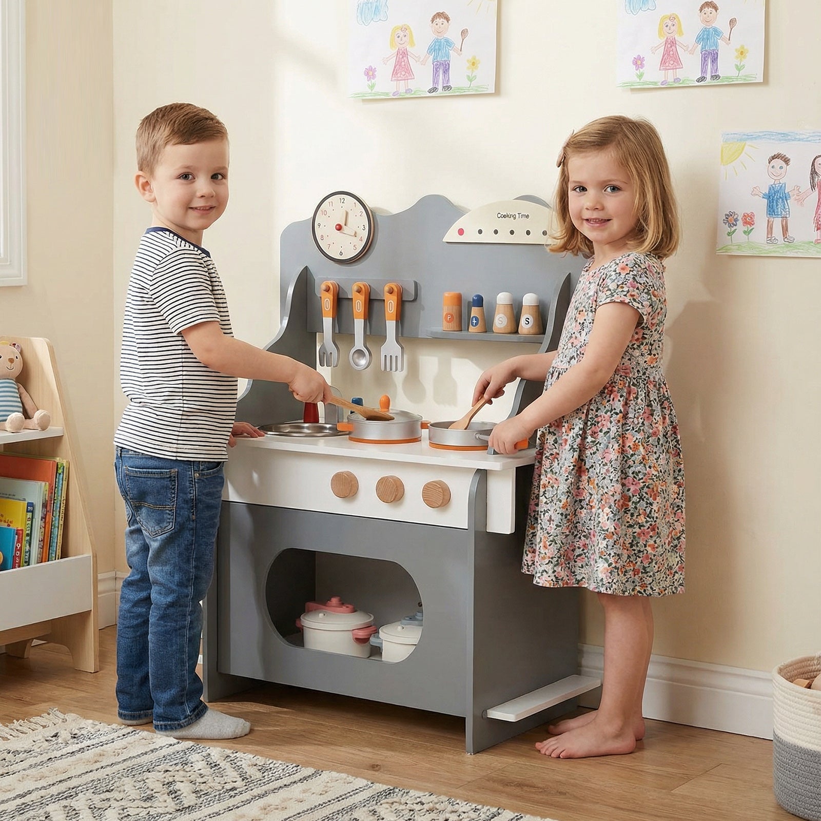 Two children playing with a toy kitchen set in a room with educational posters on the wall.