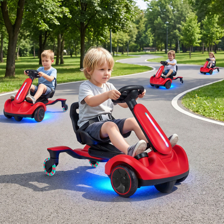A young blonde boy drives a red and black pedal kick scooter with glowing blue LED lights on a paved park path, with other children riding red kick scooters in the background.