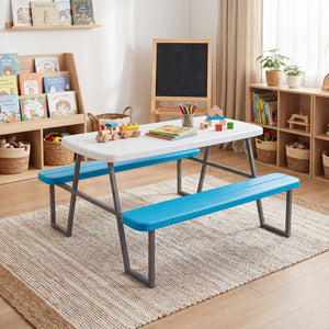 Children's play area with a white table and blue benches in a room with bookshelves and toys.