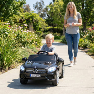 Child in a toy Mercedes-Benz car being pushed by an adult in a garden setting
