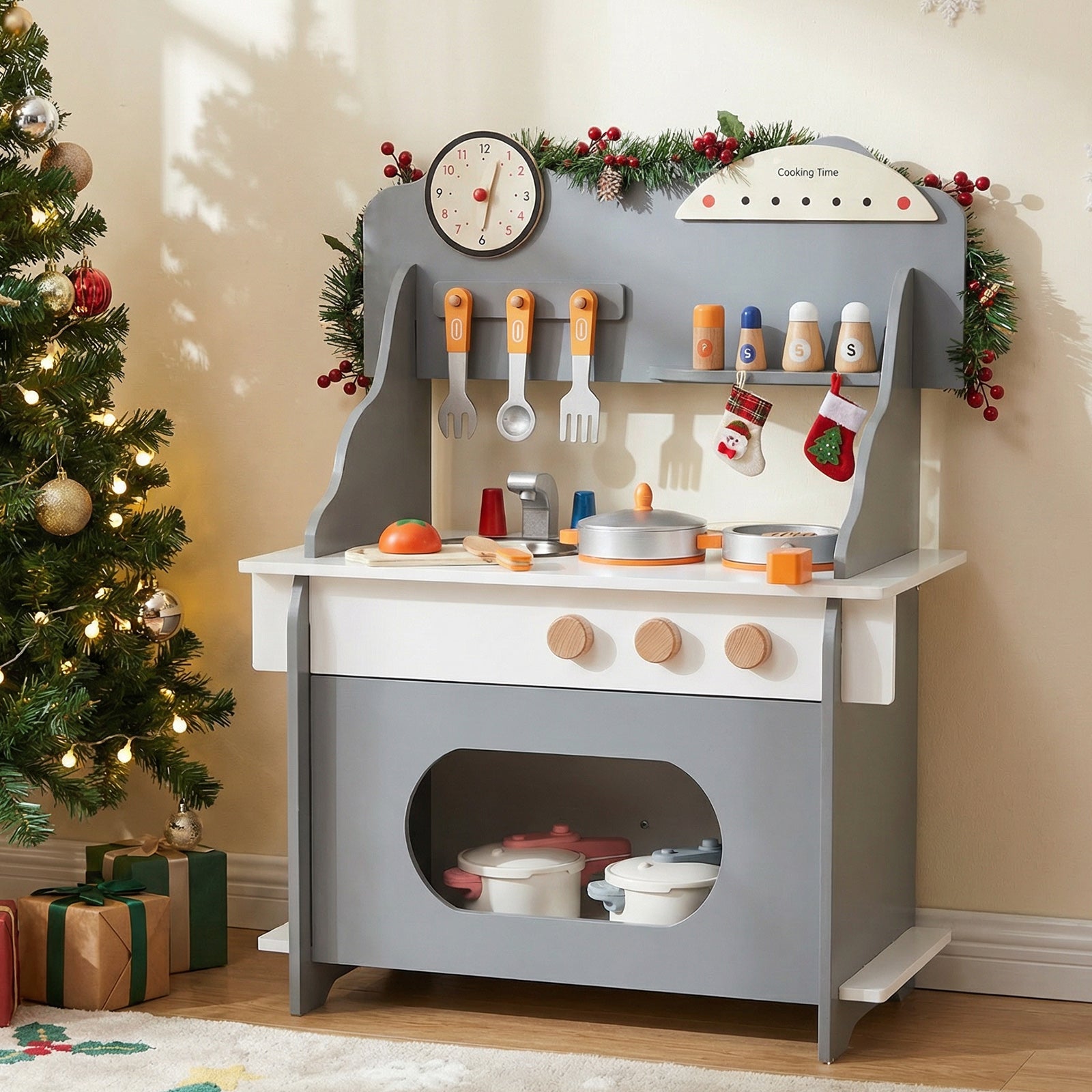 Children's play kitchen set with toy utensils and cookware, Christmas tree and decorations in the background.