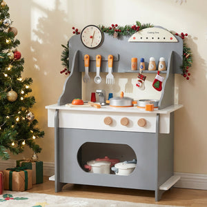Children's play kitchen set with toy utensils and cookware, Christmas tree and decorations in the background.