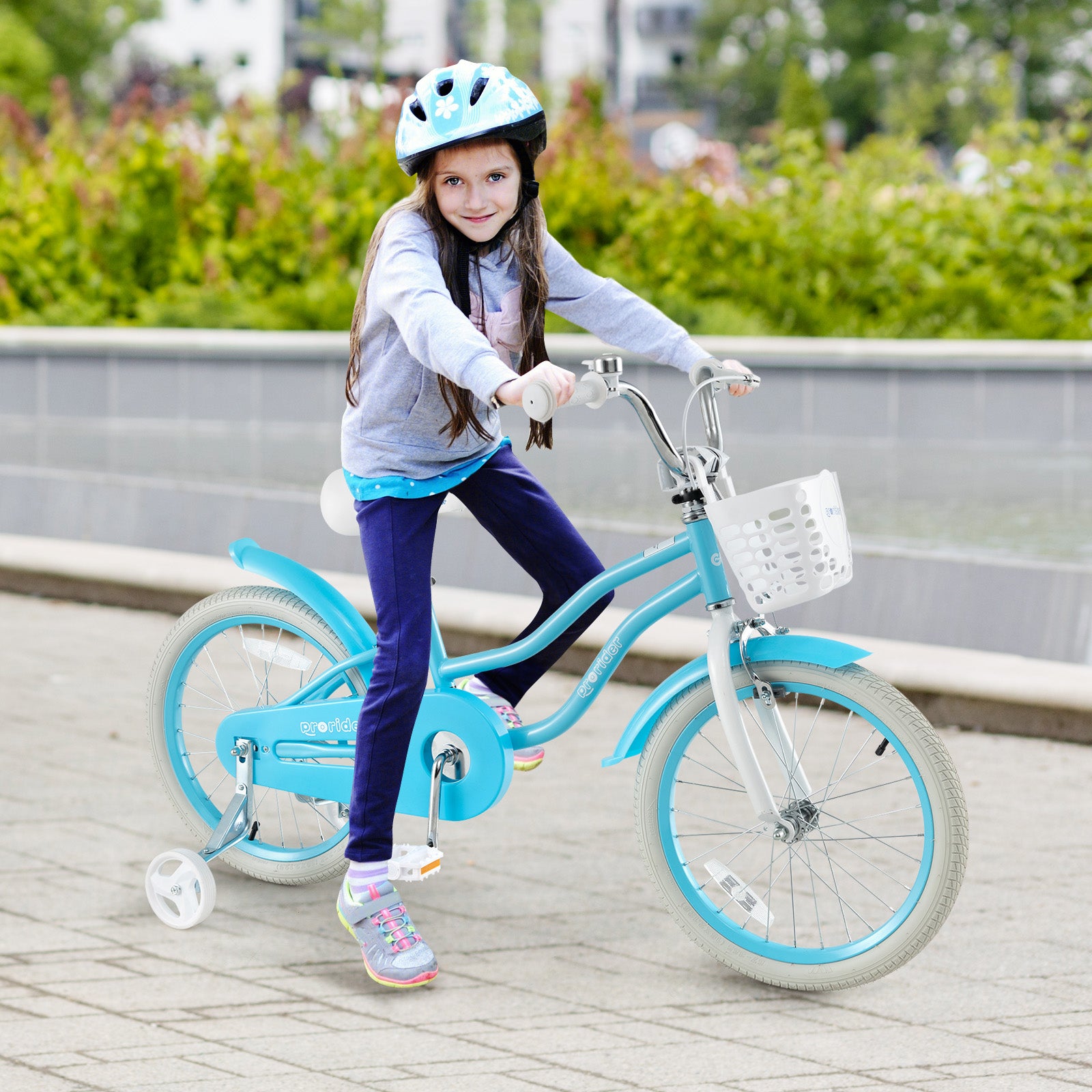 Young girl riding a blue children's bike with training wheels in an outdoor setting.