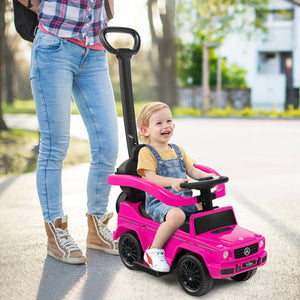 Child in a pink toy car with a person standing nearby on a road.
