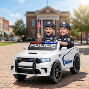 Two young children dressed as police officers sitting in a white ride-on toy car styled like a police SUV, parked on a brick street in front of a police station building.