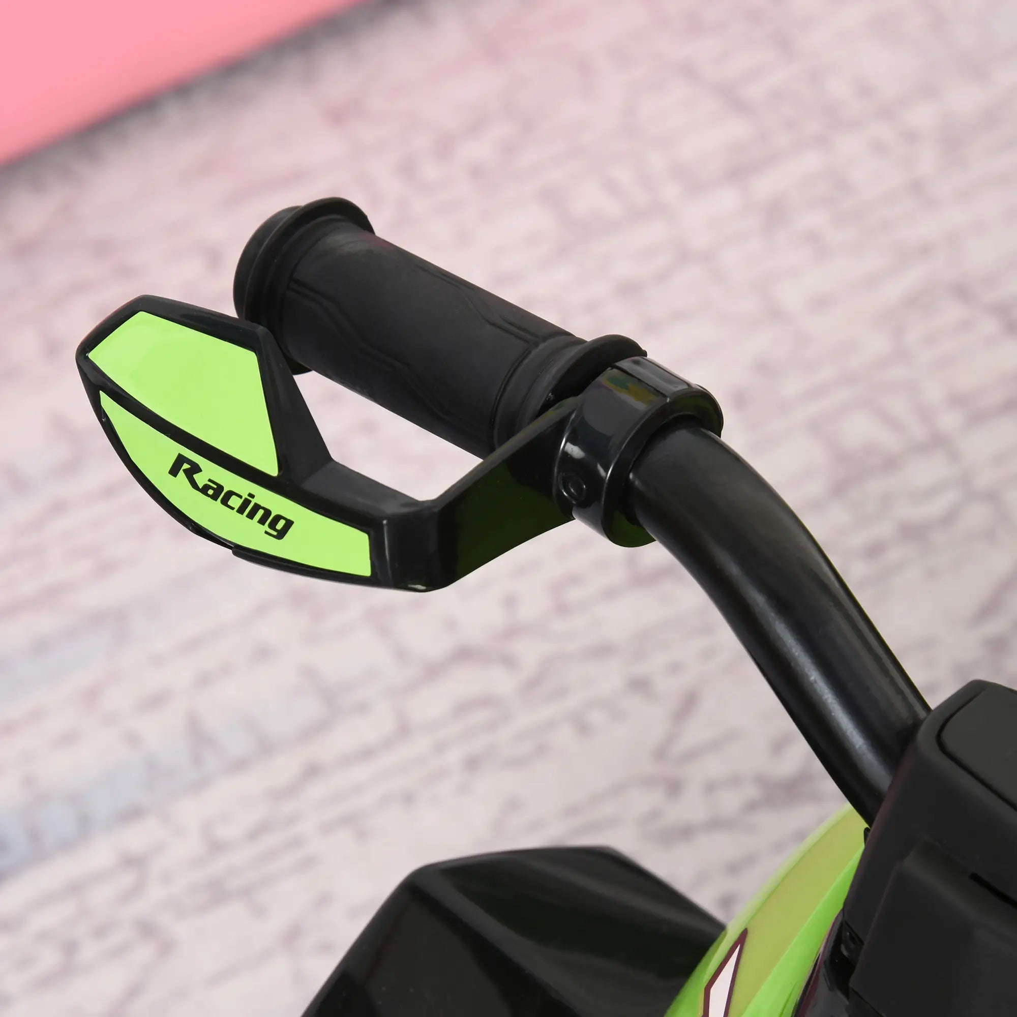 Close-up of motorcycle handlebar with green 'Racing' grips on a textured surface.