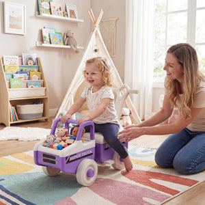 Woman and child playing with a purple toy truck in a room with a teepee and books.