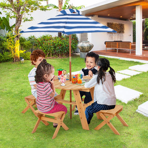 Children sitting at a wooden table under a blue and white striped umbrella in a garden setting.