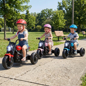 Three children riding toy motorcycles on a sidewalk with trees in the background