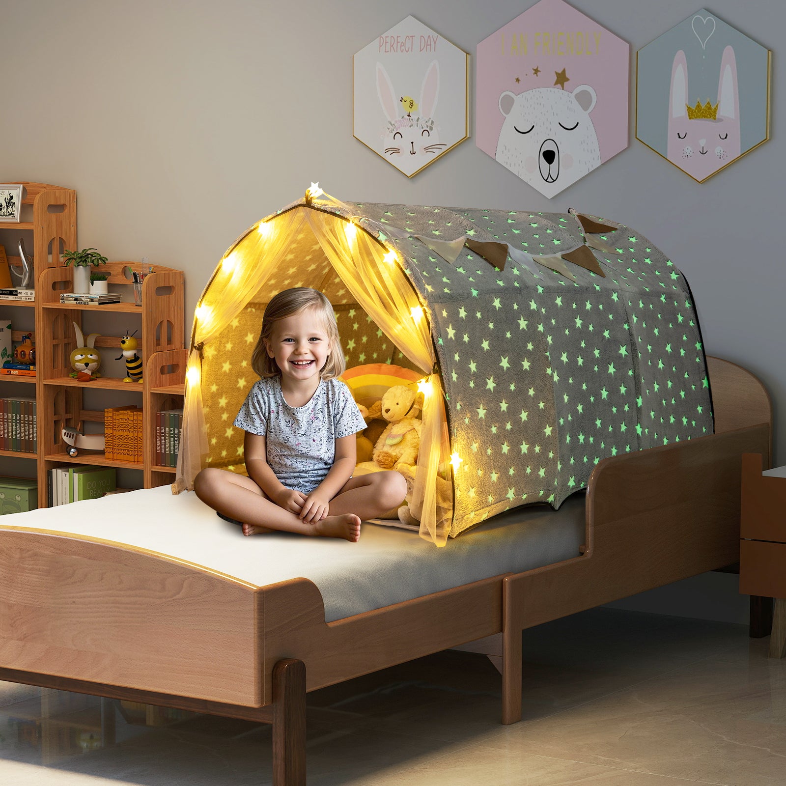 Child sitting inside a lit children's tent on a bed in a room with decorative wall art.
