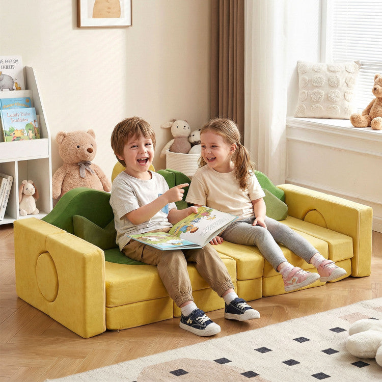 Two children sitting on a yellow and green kids' sofa in a room with toys and books.