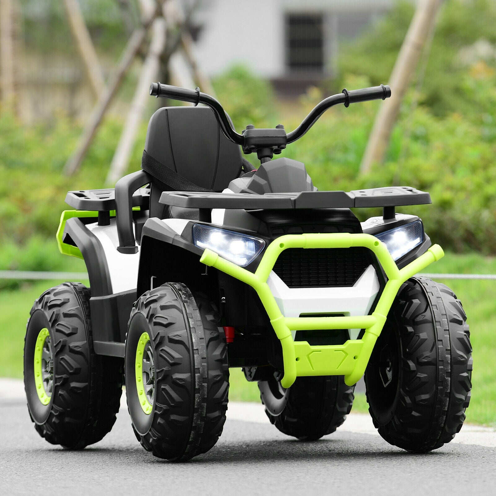 Children's green and black ATV on a paved surface with grass and trees in the background
