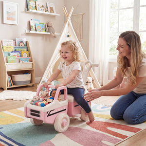 Woman and child playing with a pink toy car in a room with a teepee and books.