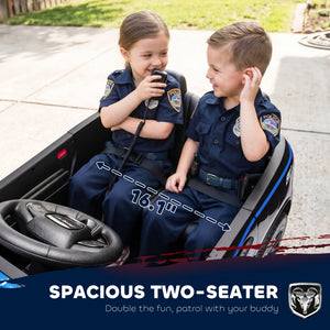 Two children wearing navy blue police uniforms sitting in a black ride-on toy car outdoors. The image includes a text banner at the bottom that reads 'SPACIOUS TWO-SEATER' and shows a Ram logo.