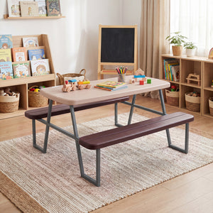 Children's play area with a wooden table and benches in a room with bookshelves and toys.