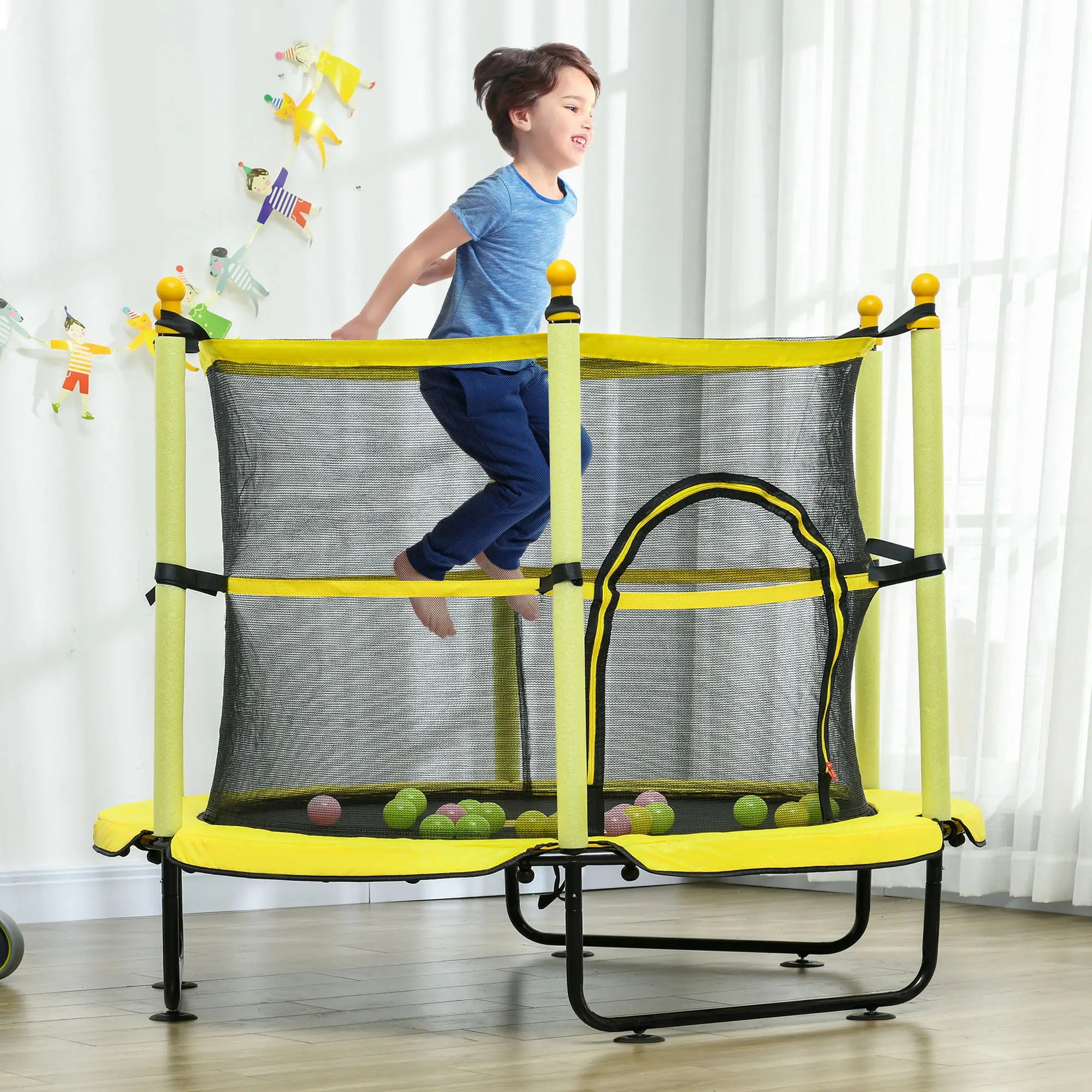 Child playing on a yellow and black trampoline with safety net in a room.