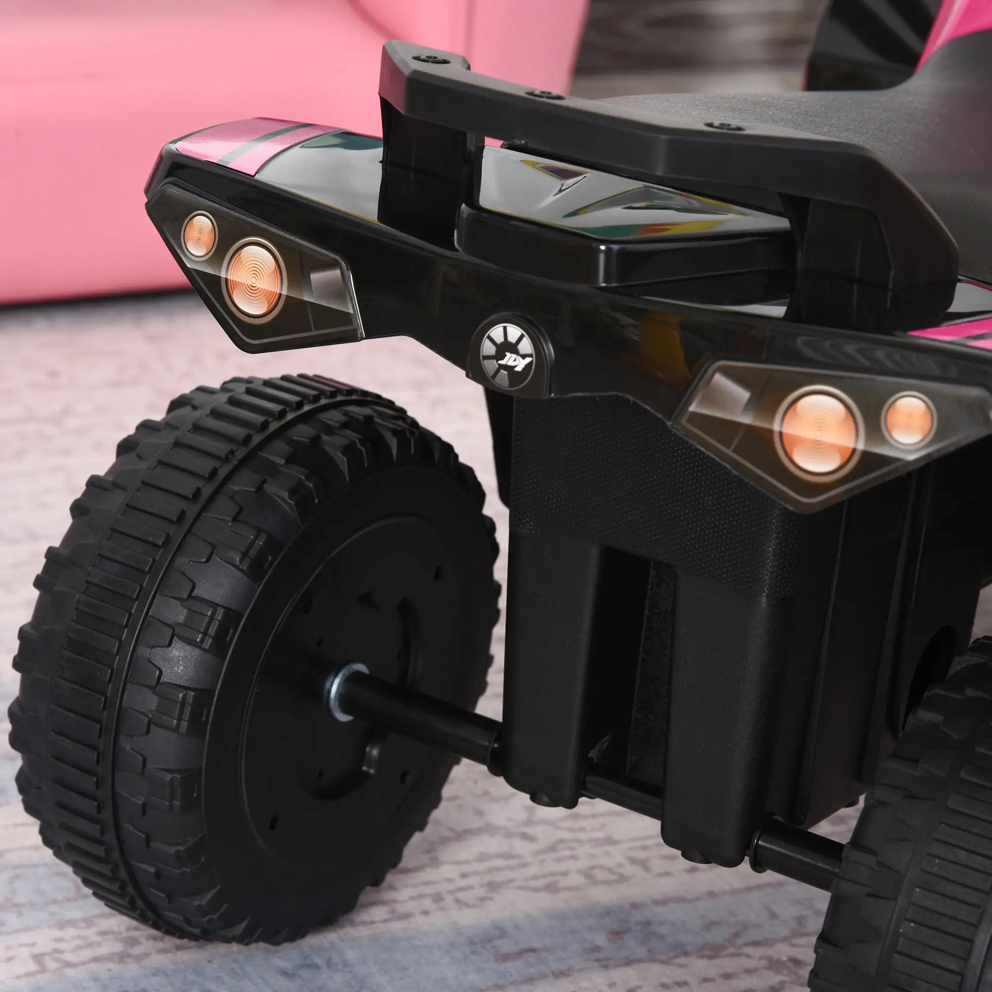 Close-up of a toy vehicle with black wheels and lights on a patterned surface.