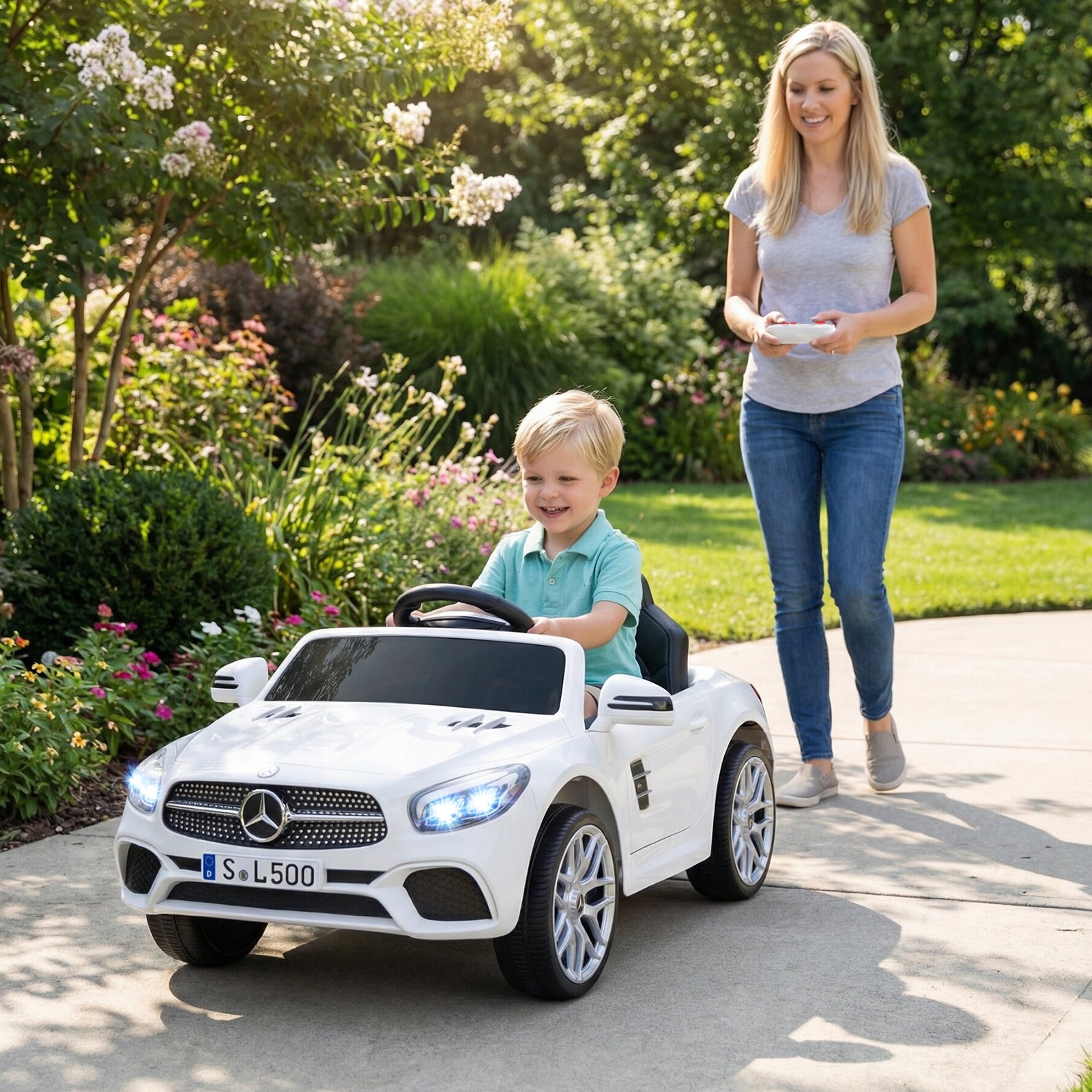 Child in a toy Mercedes-Benz car being pushed by an adult in a garden.