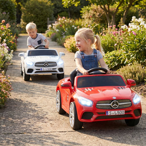 Two children driving toy Mercedes-Benz cars on a garden path.