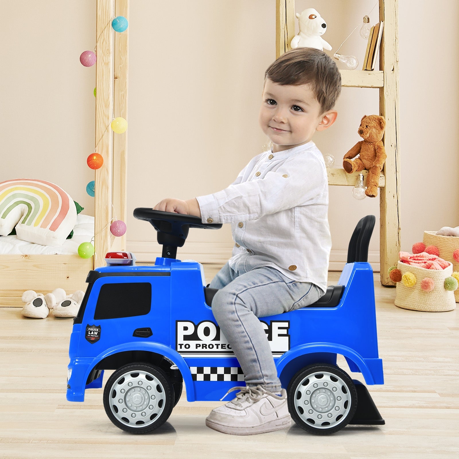 Child sitting on a blue toy police car in a room with toys and decorations.