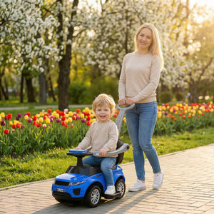 Woman and child in a blue toy car in a park with tulips and blooming trees.