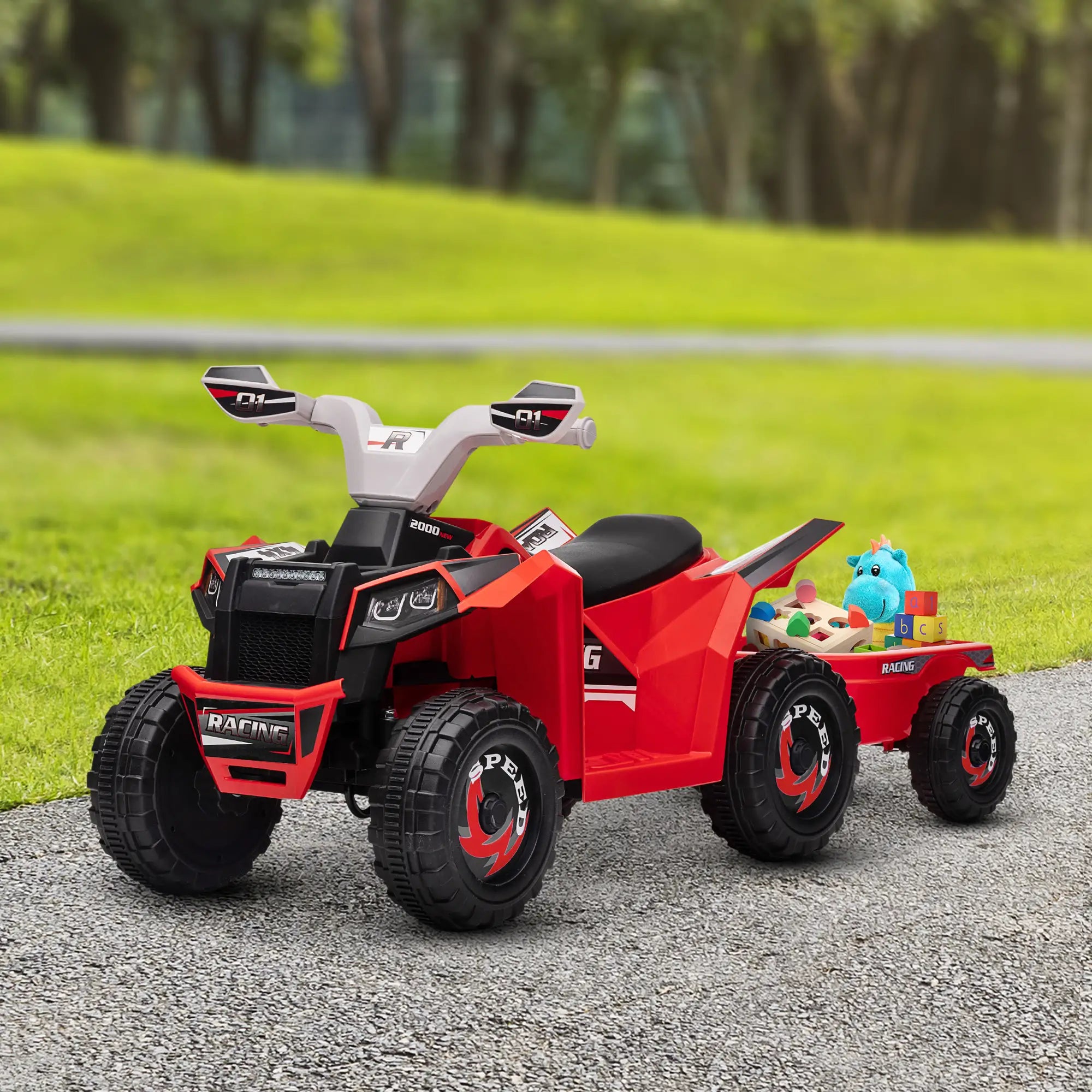 Red toy ATV with a black seat and black wheels on a gravel path with grass and trees in the background.