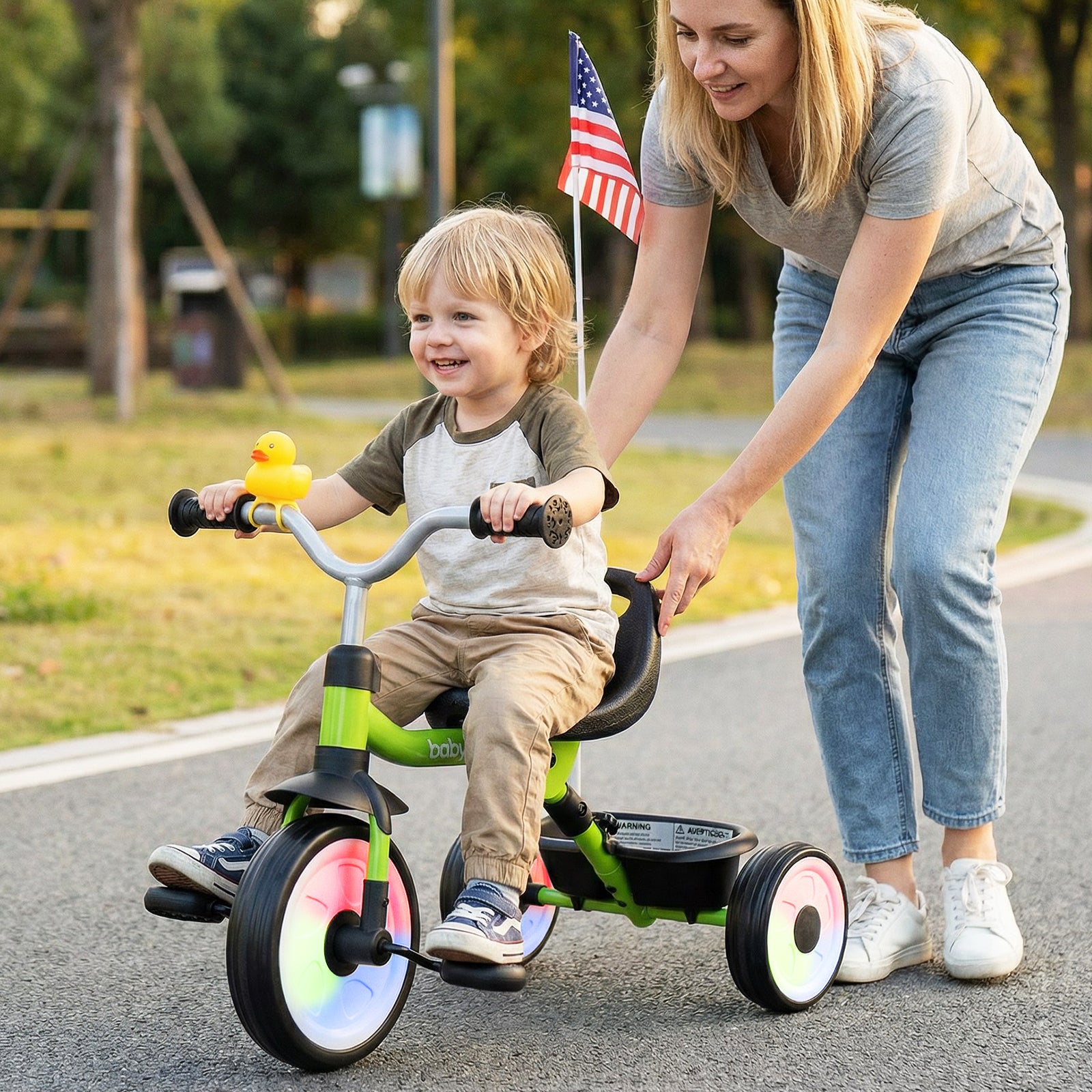 Woman pushing a child on a tricycle with a American flag in the background