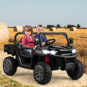 Children sitting in a black toy off-road vehicle in a field with hay bales.