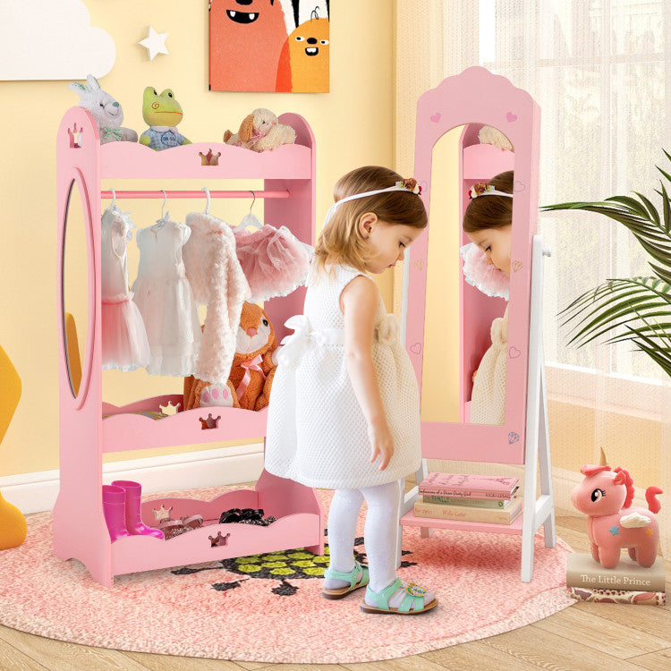 Child in a white dress standing in front of a pink toy wardrobe and mirror in a room with toys and decorations.