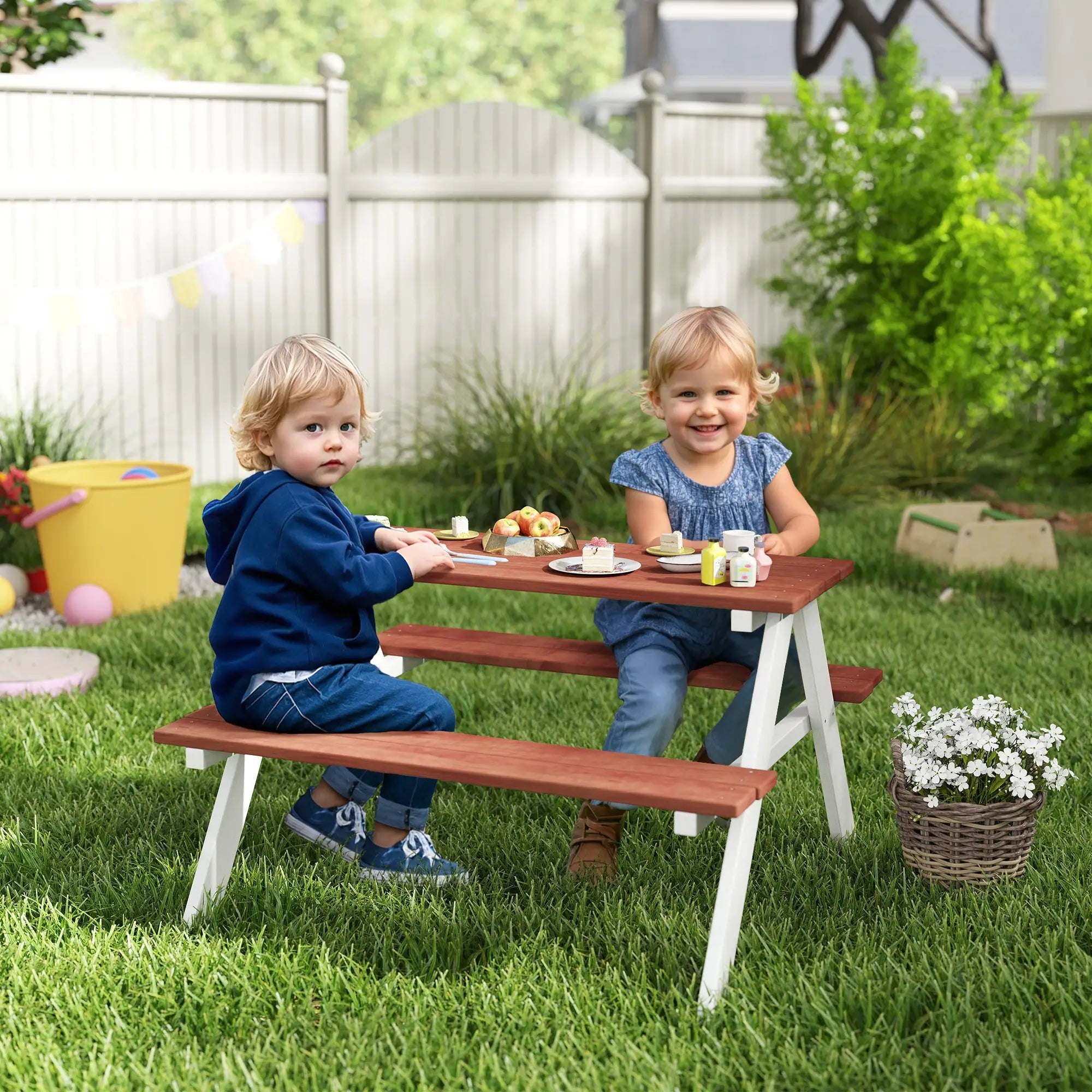 Two children sitting at a wooden picnic table in a backyard setting.
