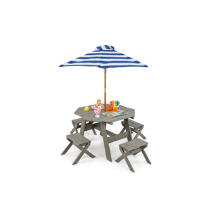 A miniature gray wooden picnic table set with a blue and white striped umbrella, small toy chairs, and colorful toy fruit and drink accessories on a plain white background.
