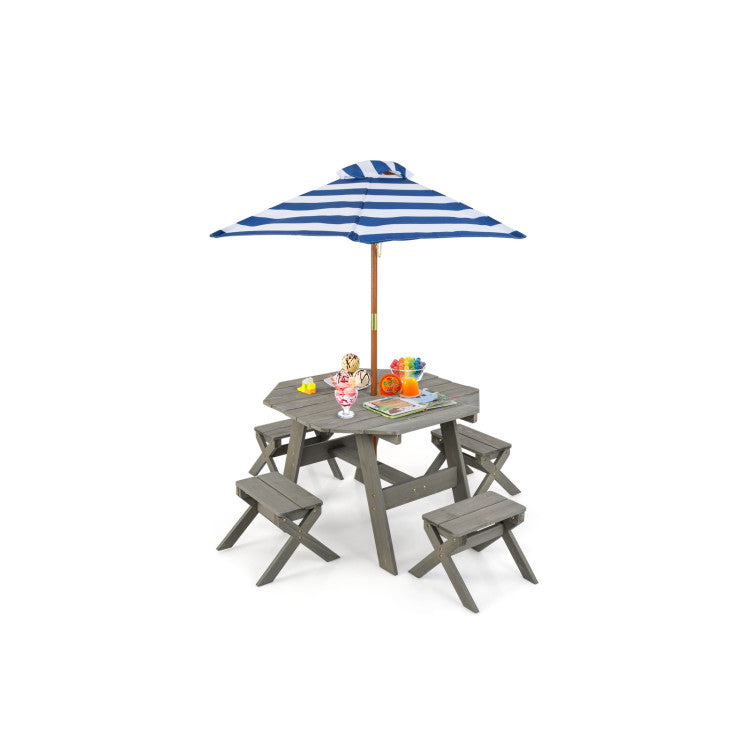A miniature gray wooden picnic table set with a blue and white striped umbrella, small toy chairs, and colorful toy fruit and drink accessories on a plain white background.