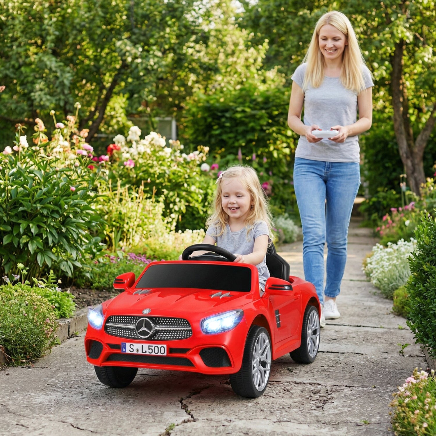 Woman pushing a child in a red toy car through a garden.