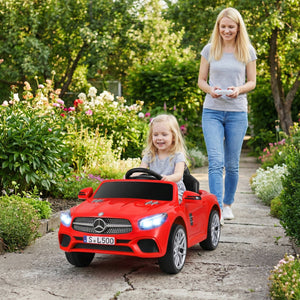 Woman pushing a child in a red toy car through a garden.