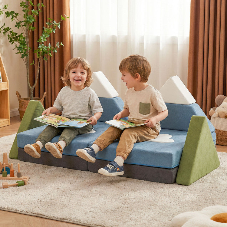 Two children sitting on a blue and green wedge-shaped sofa in a room with curtains and toys.