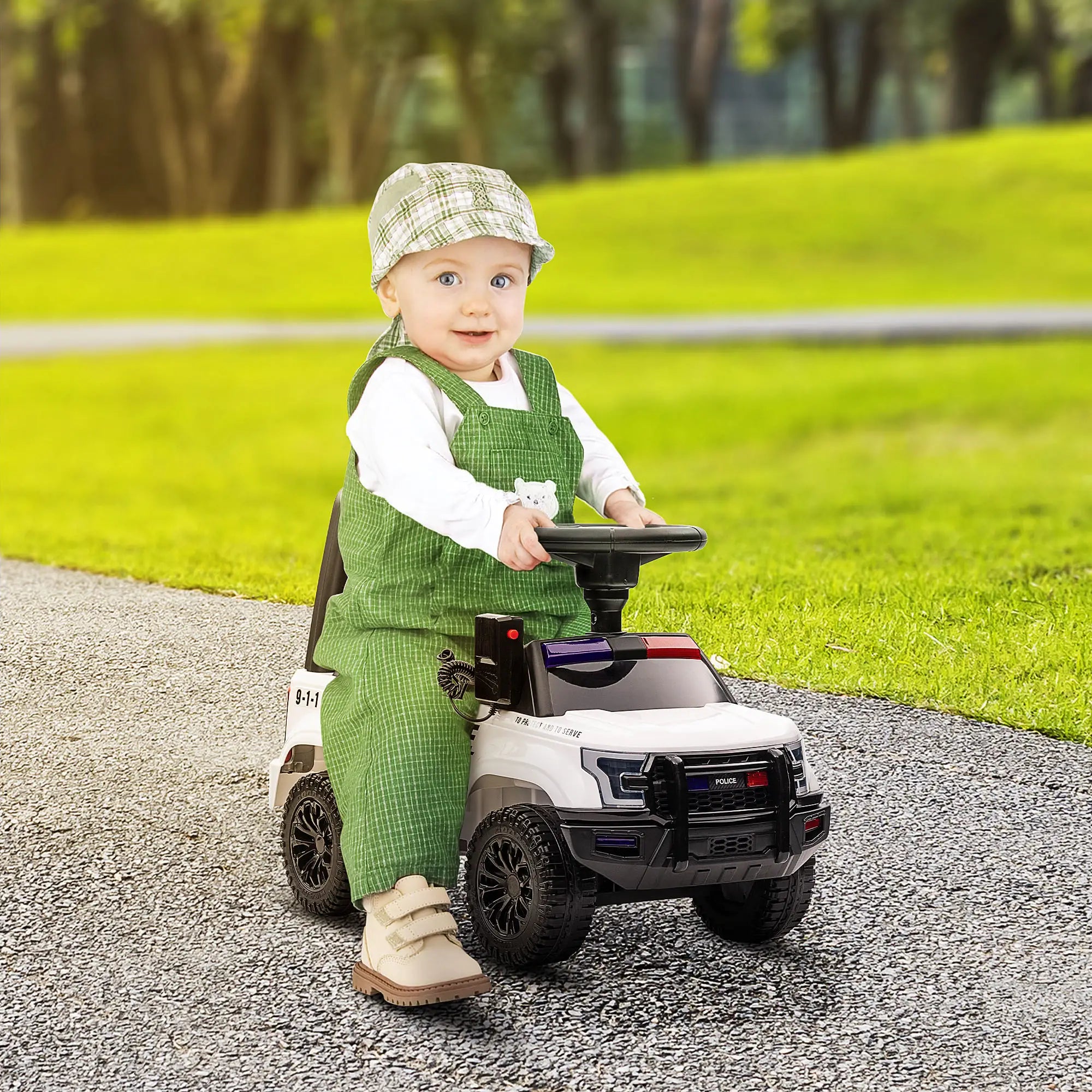 Child in green outfit and cap riding a toy car on a path with grass and trees in the background