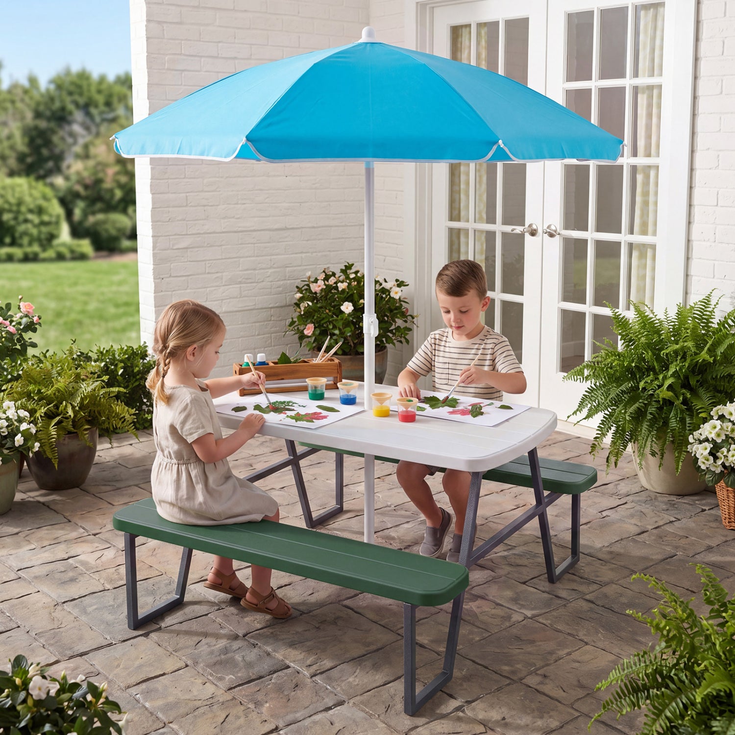 Two children sitting at a picnic table with a blue umbrella on a patio.