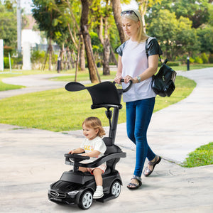 Woman pushing a child in a toy car along a path in a park.