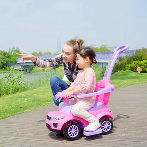 Woman and child riding a pink toy car outdoors on a wooden path.