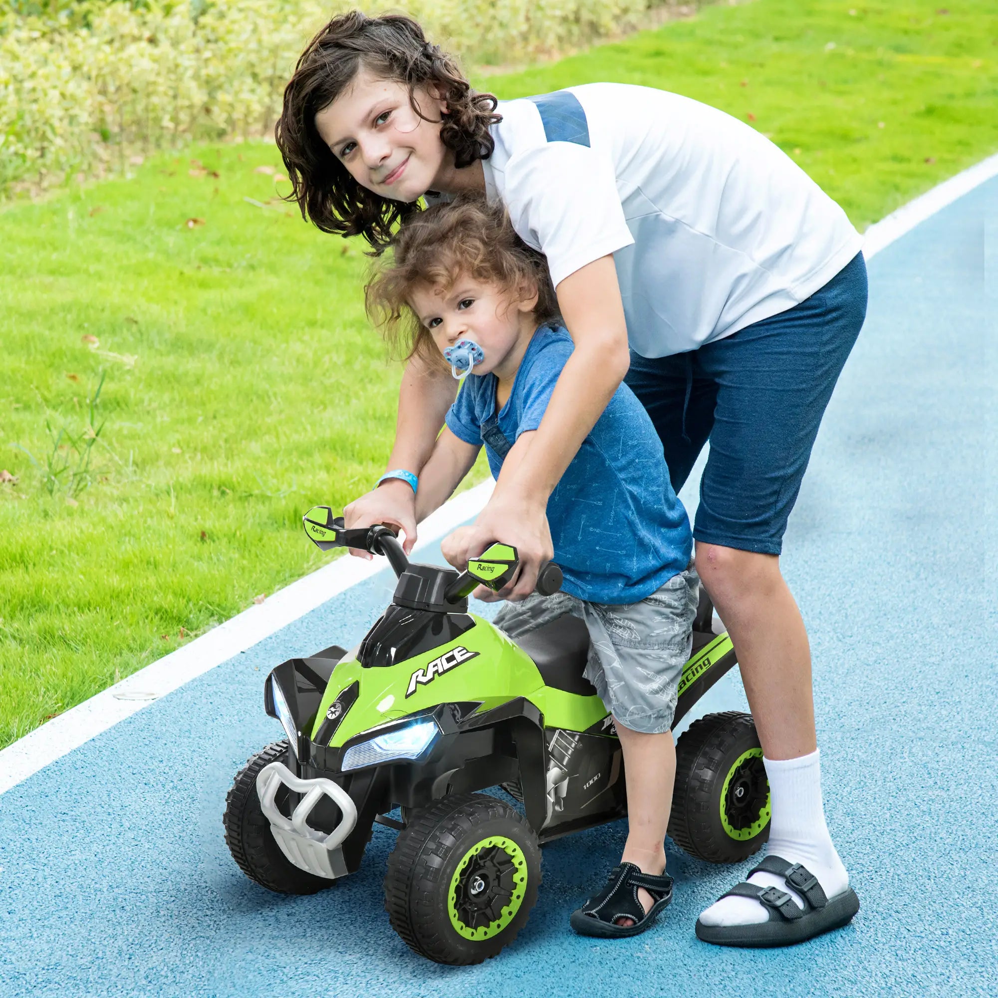 Two children playing with a green toy car on a blue path with grass in the background