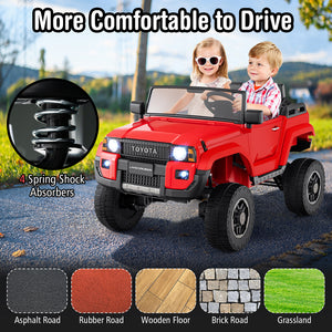 Red toy car with children driving it, featuring 4 spring shock absorbers, on a road with grass and trees in the background.