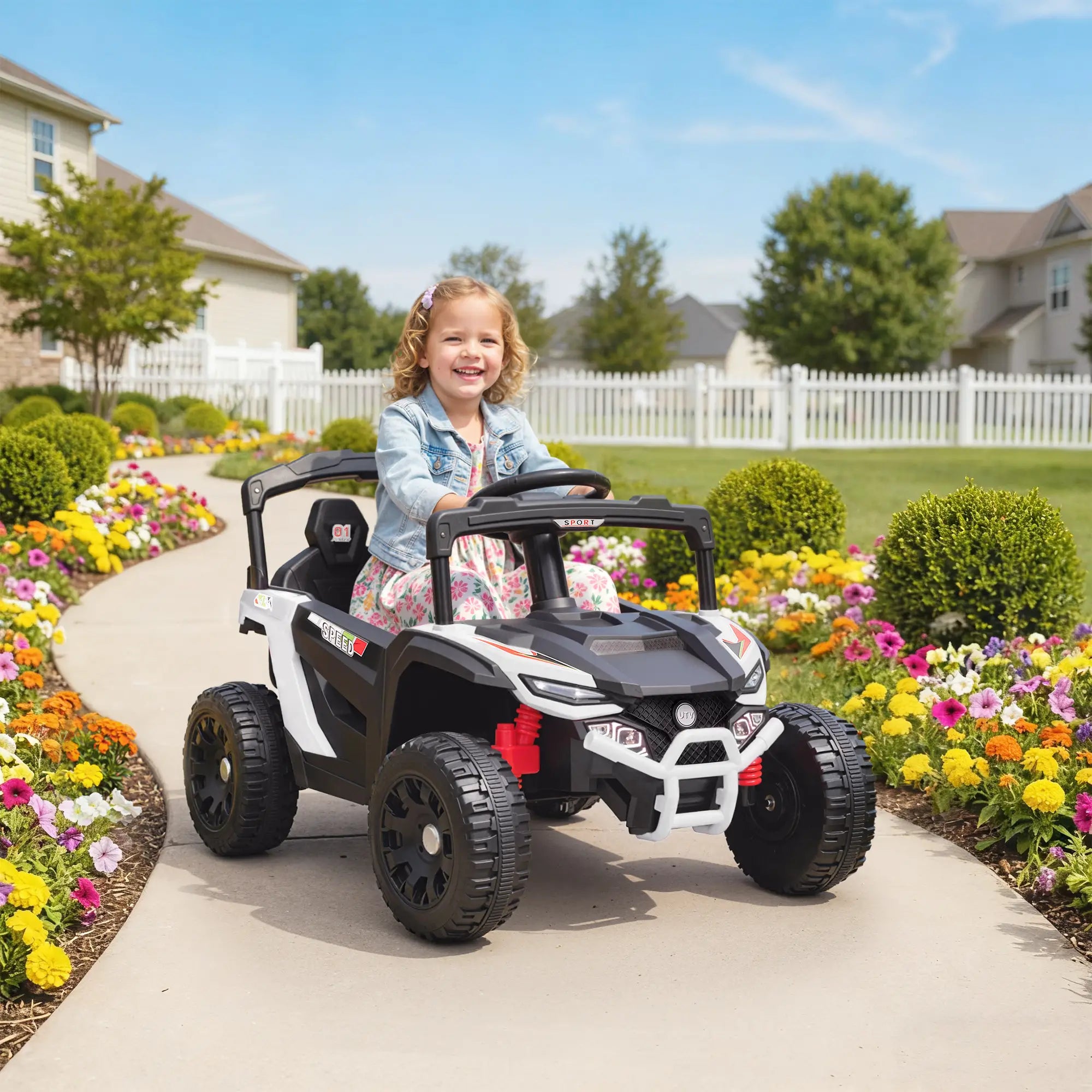 Child in a toy car on a sidewalk with a garden and houses in the background