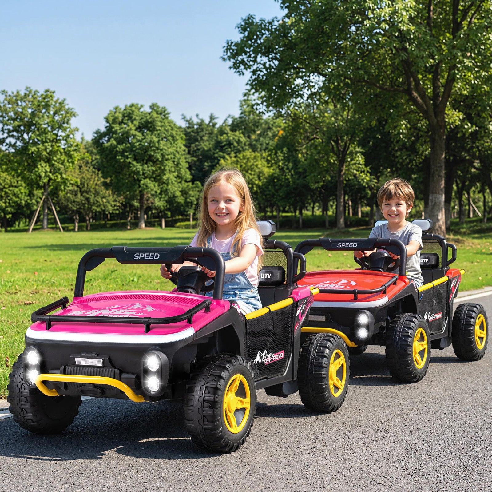 Two children sitting in toy cars on a road with trees in the background