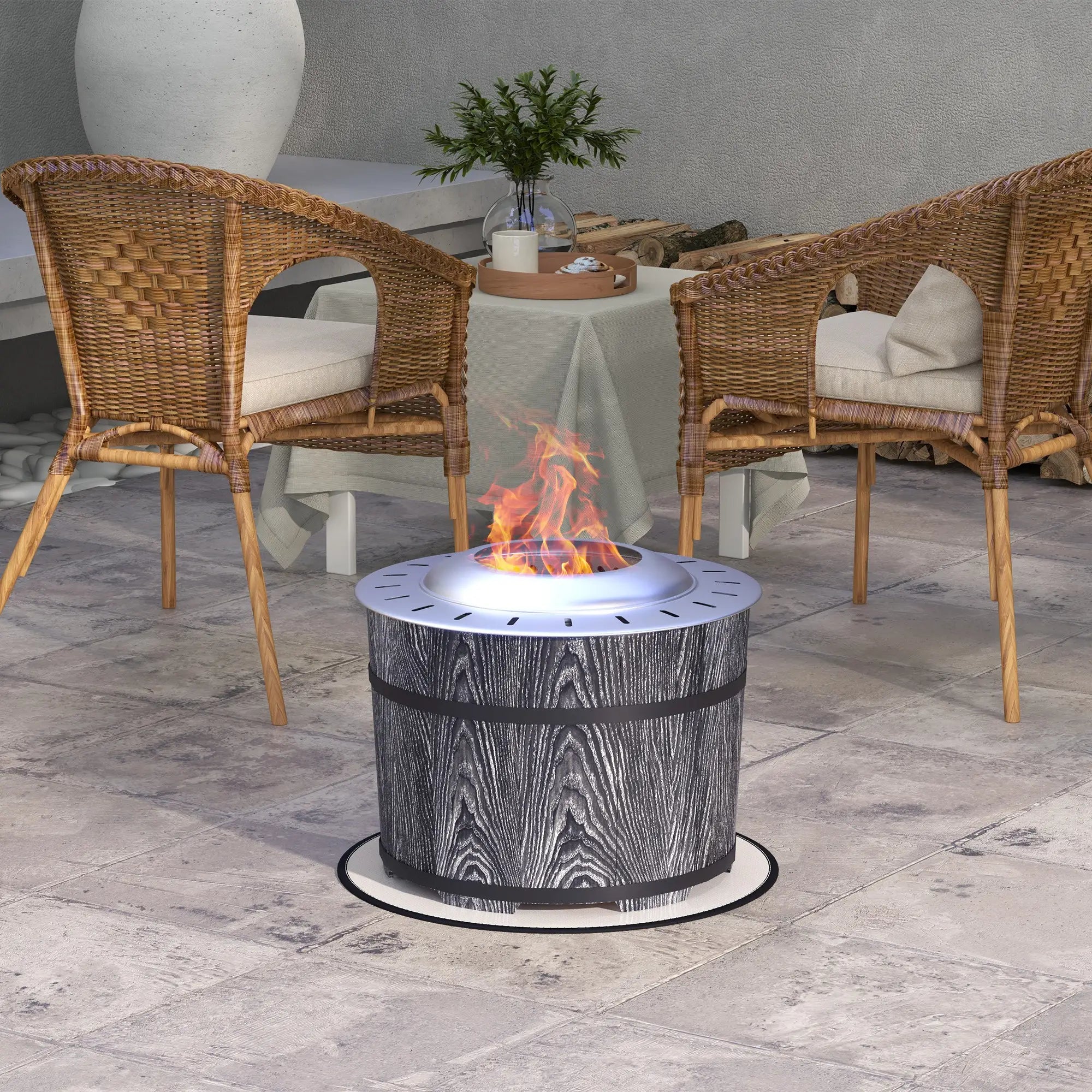 A round outdoor fire pit table with a gray wood-grain pattern and black bands, shown lit with flames in a patio setting between two wicker chairs.