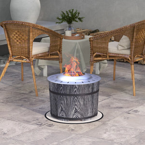 A round outdoor fire pit table with a gray wood-grain pattern and black bands, shown lit with flames in a patio setting between two wicker chairs.