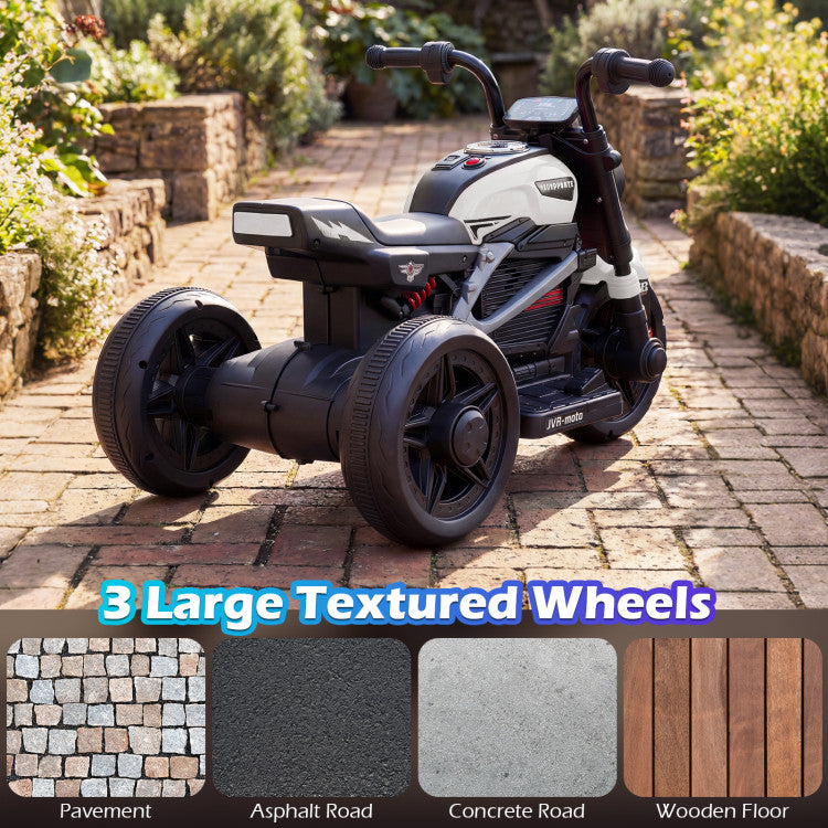 Children's electric trike with large textured wheels on a brick path, surrounded by greenery.