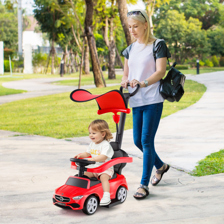 Woman pushing a child in a red toy car on a sidewalk with trees in the background